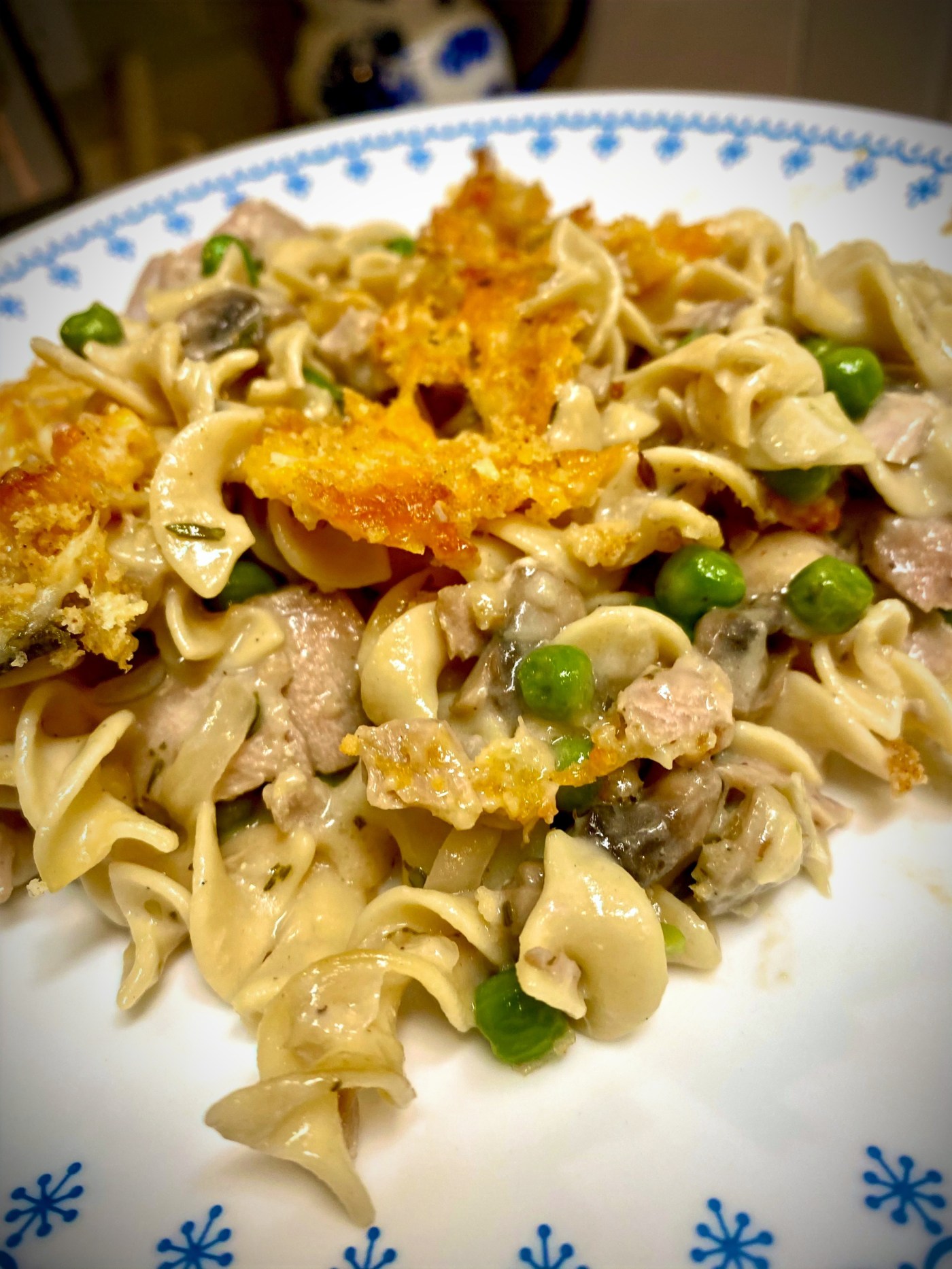 A golden-baked tuna casserole topped with melted cheese and crispy panko, served in a white ceramic baking dish with parsley garnish.