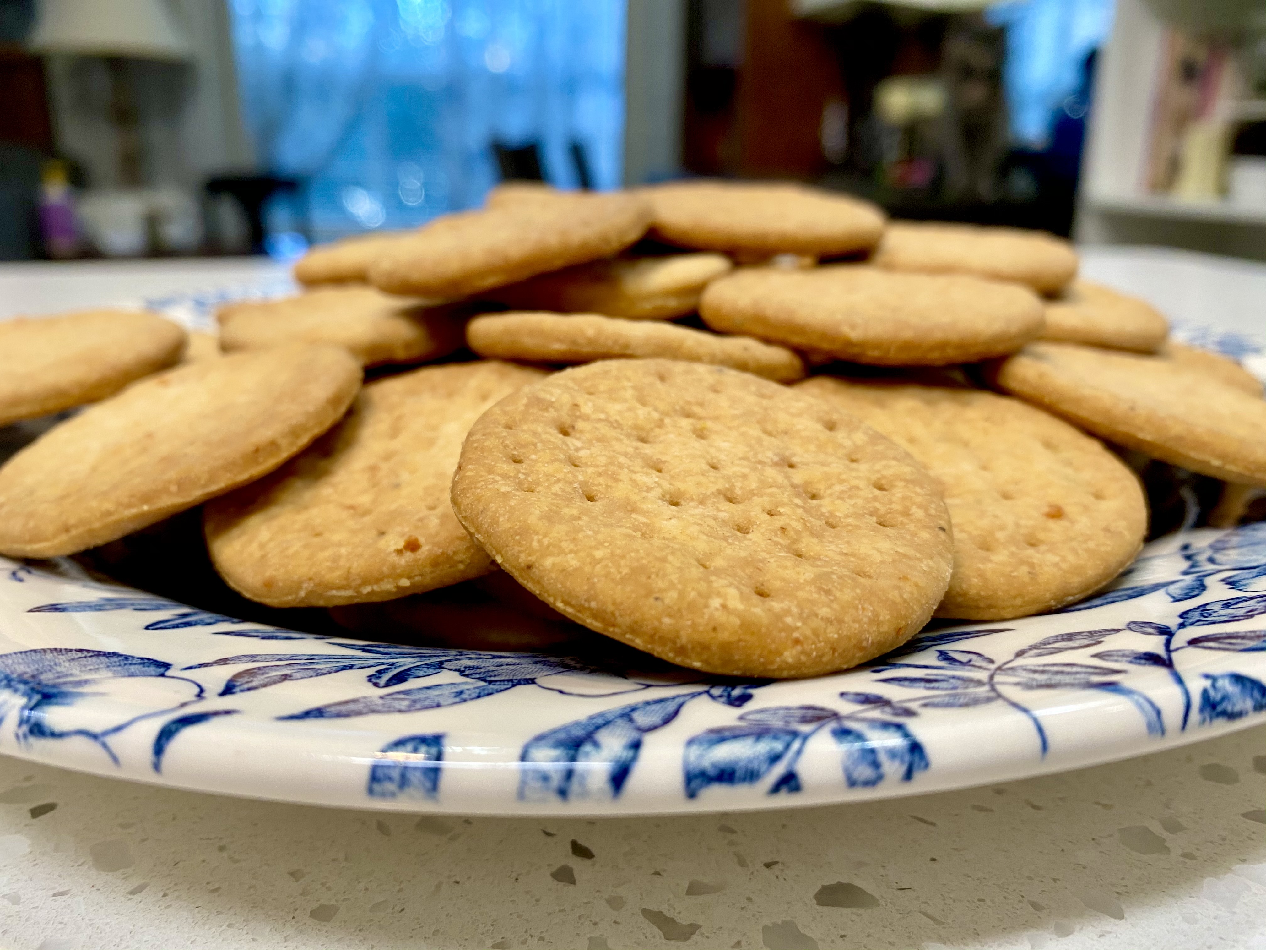 Crisp olive oil crackers stacked on a blue and white ceramic plate in a cozy kitchen setting.