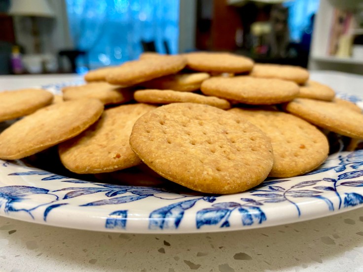 Crisp olive oil crackers stacked on a blue and white ceramic plate in a cozy kitchen setting.