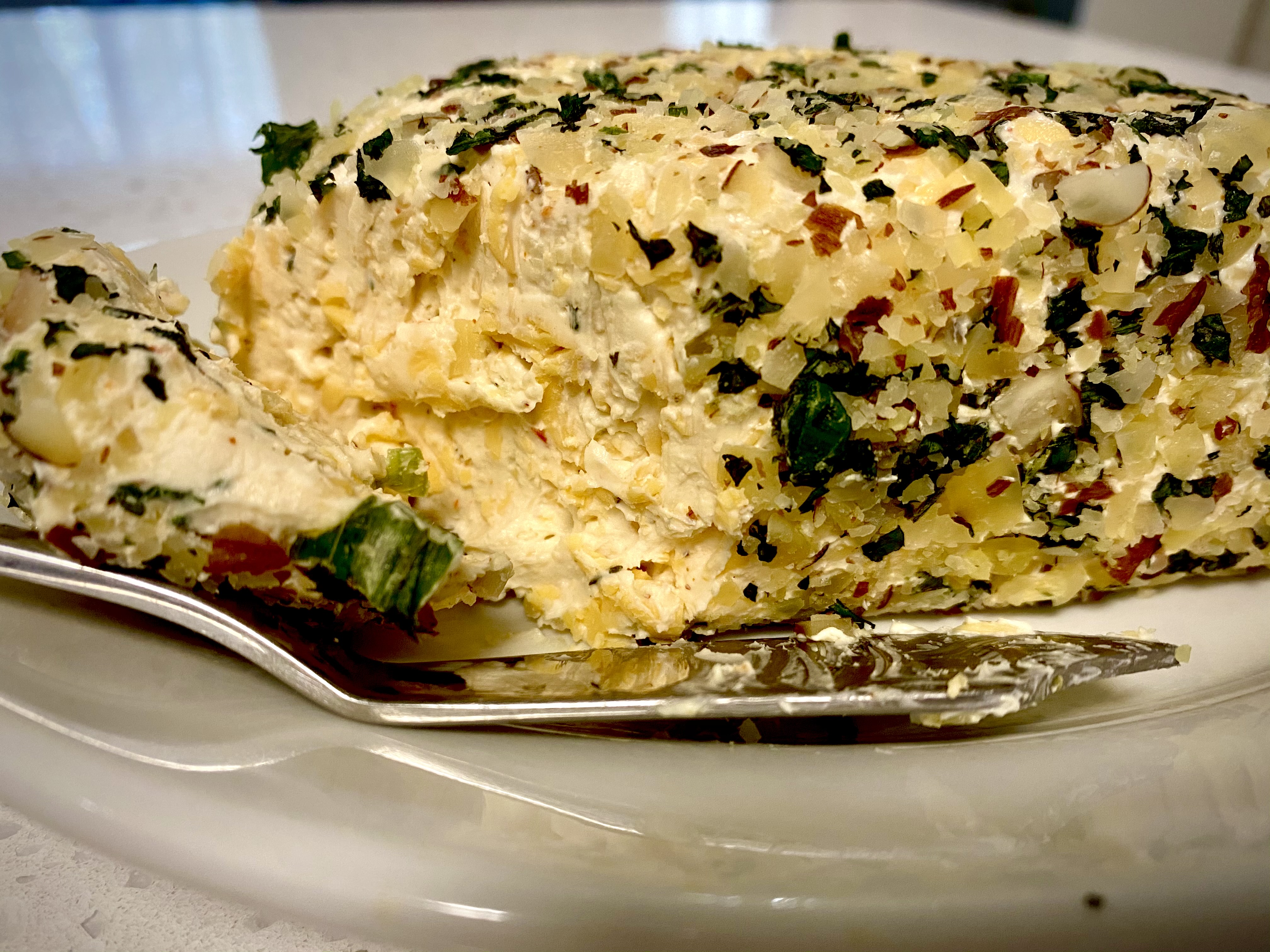 A vibrant cheeseball coated in herbs and crushed almonds, served on a vintage platter with crisp olive oil crackers.