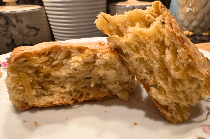 Interior view of a split caramelized onion and cheddar scone, showcasing soft, flaky layers.