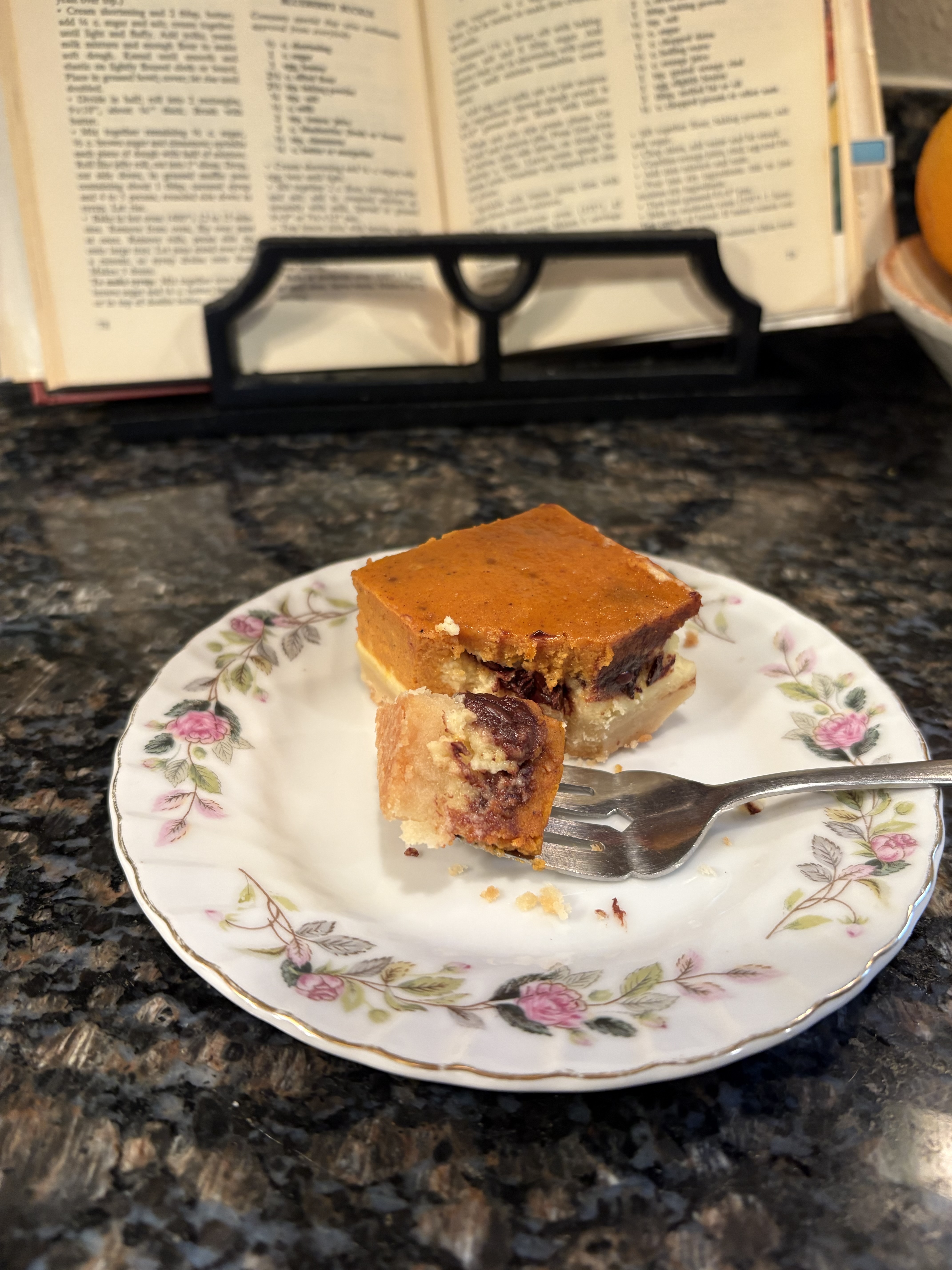 Pumpkin cheesecake chocolate chip bar with visible layers of shortbread crust, cheesecake, melted chocolate, and pumpkin custard on a vintage floral plate