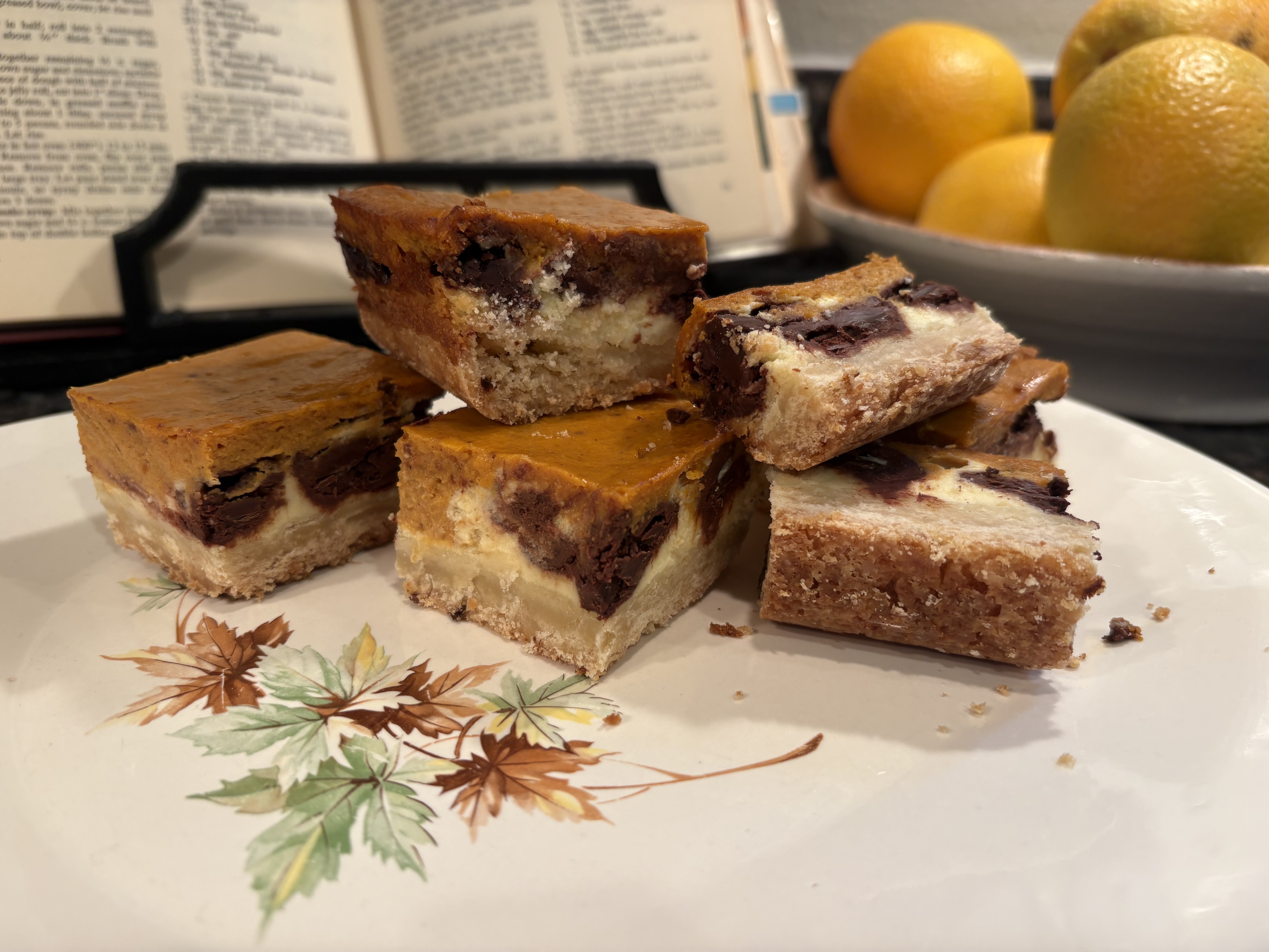 Pumpkin cheesecake chocolate chip bars stacked on a vintage plate beside an open cookbook