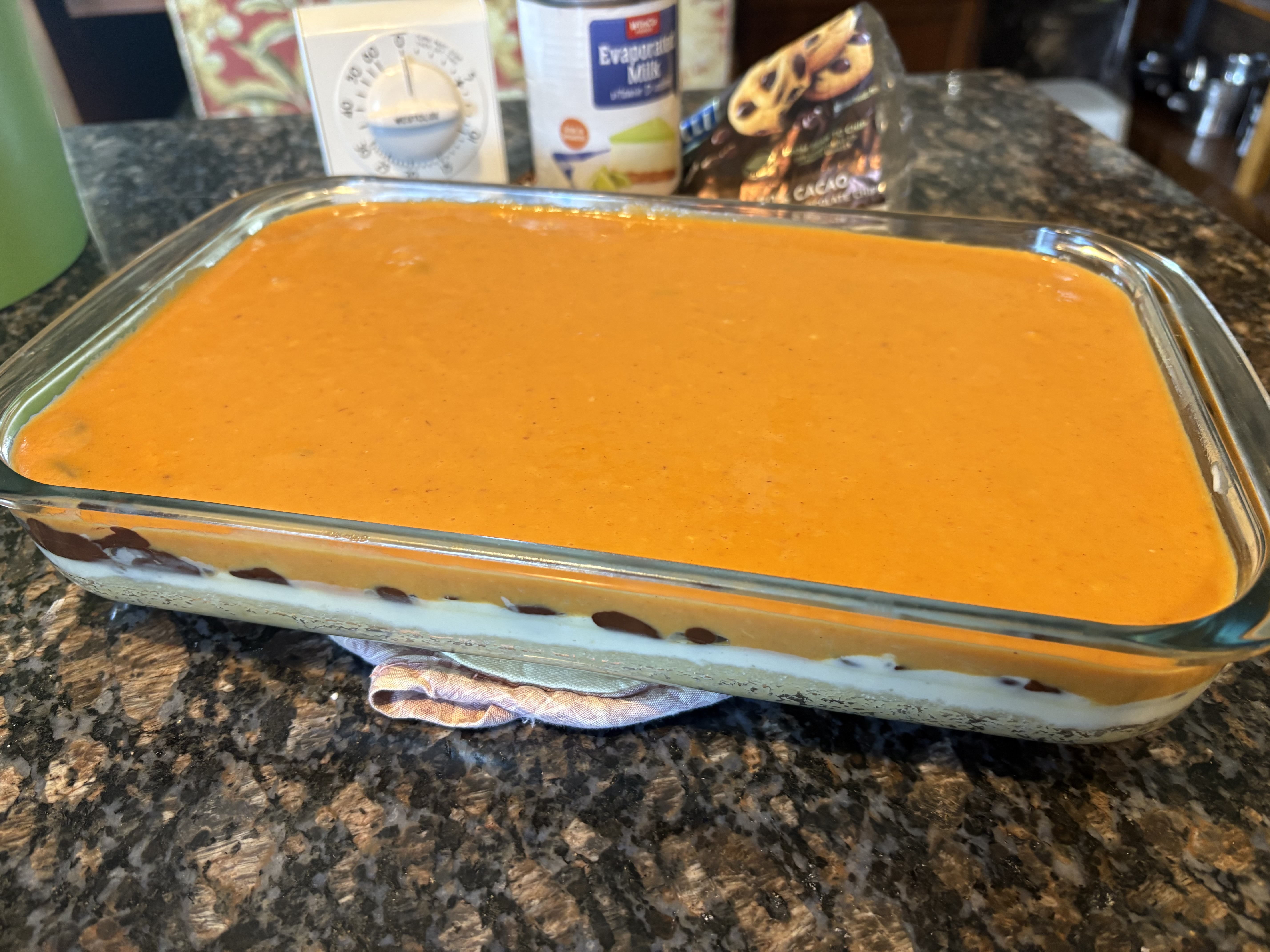 Pumpkin custard layer poured over chocolate chips, showing distinct layers before baking